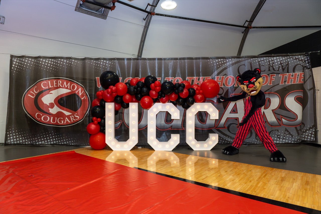 The Bearcat mascot poses near a University of Cincinnati Clermont College welcome sign