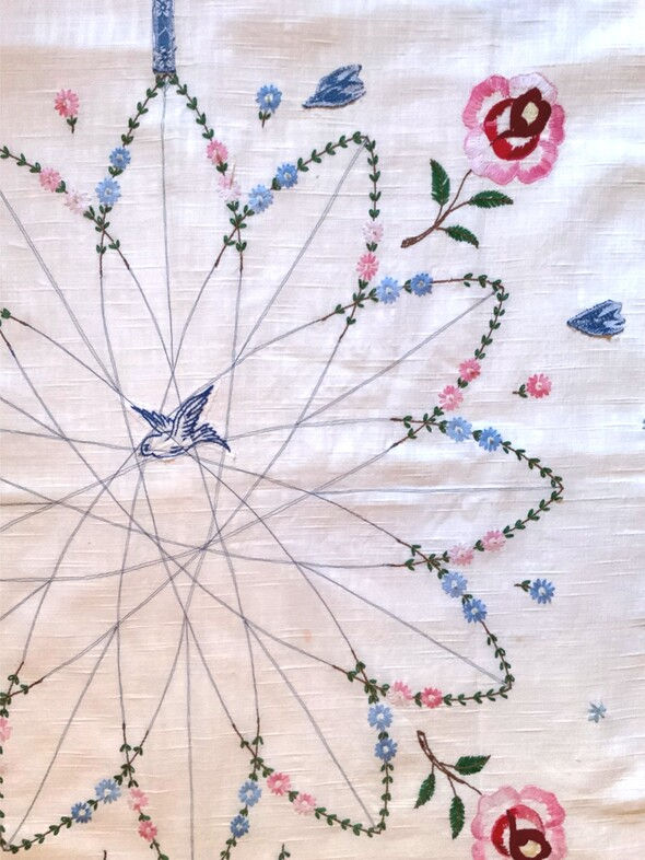 close up of a table cloth featuring an embroidered blue bird in a floral cage