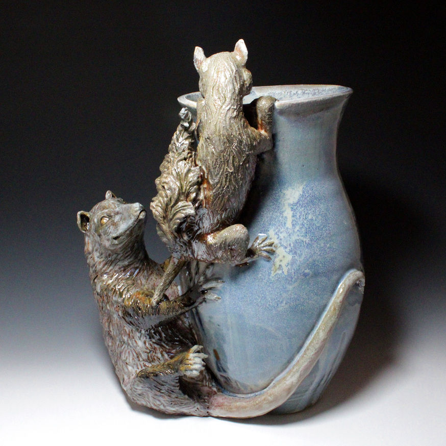 photo of a blue ceramic vase with an opossum sculpted at the bottom and a squirrel sculpted like it's climbing the vase