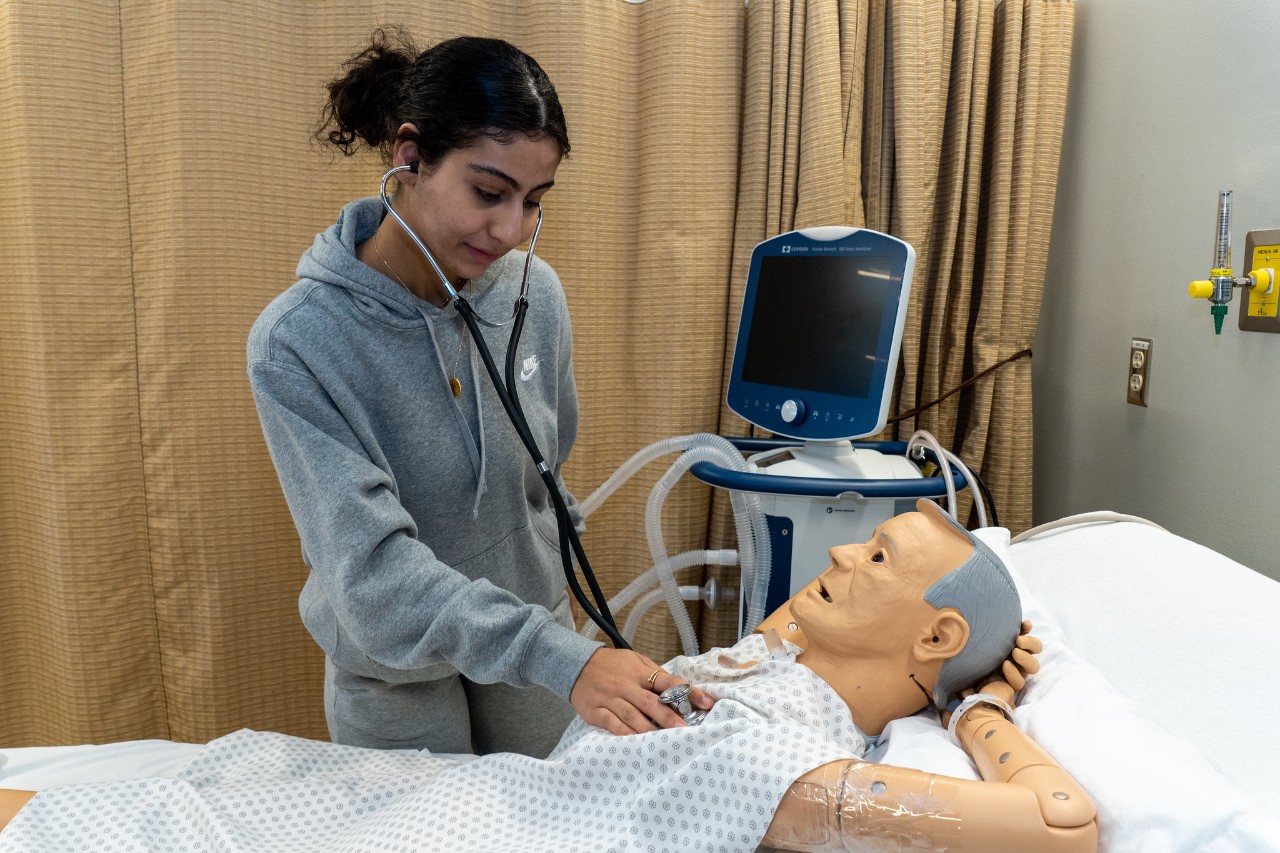 student poses with mannequin laying in a hospital bed