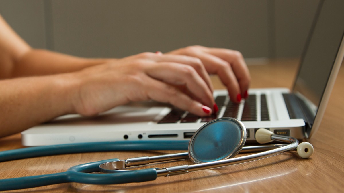 hands typing on laptop keyboard next to stethoscope