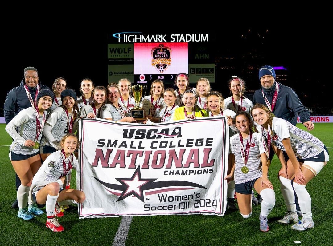 women's soccer team and coaches pose with championship banner for their second straight year