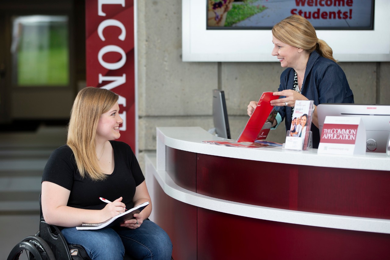 Student in a wheelchair asks for help at the welcome desk