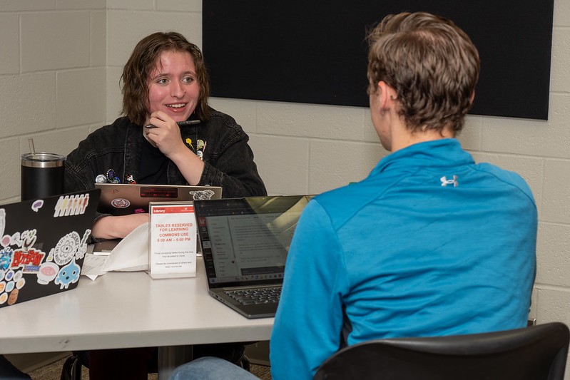 woman sits at computer smiling at camera with a skeleton next to her